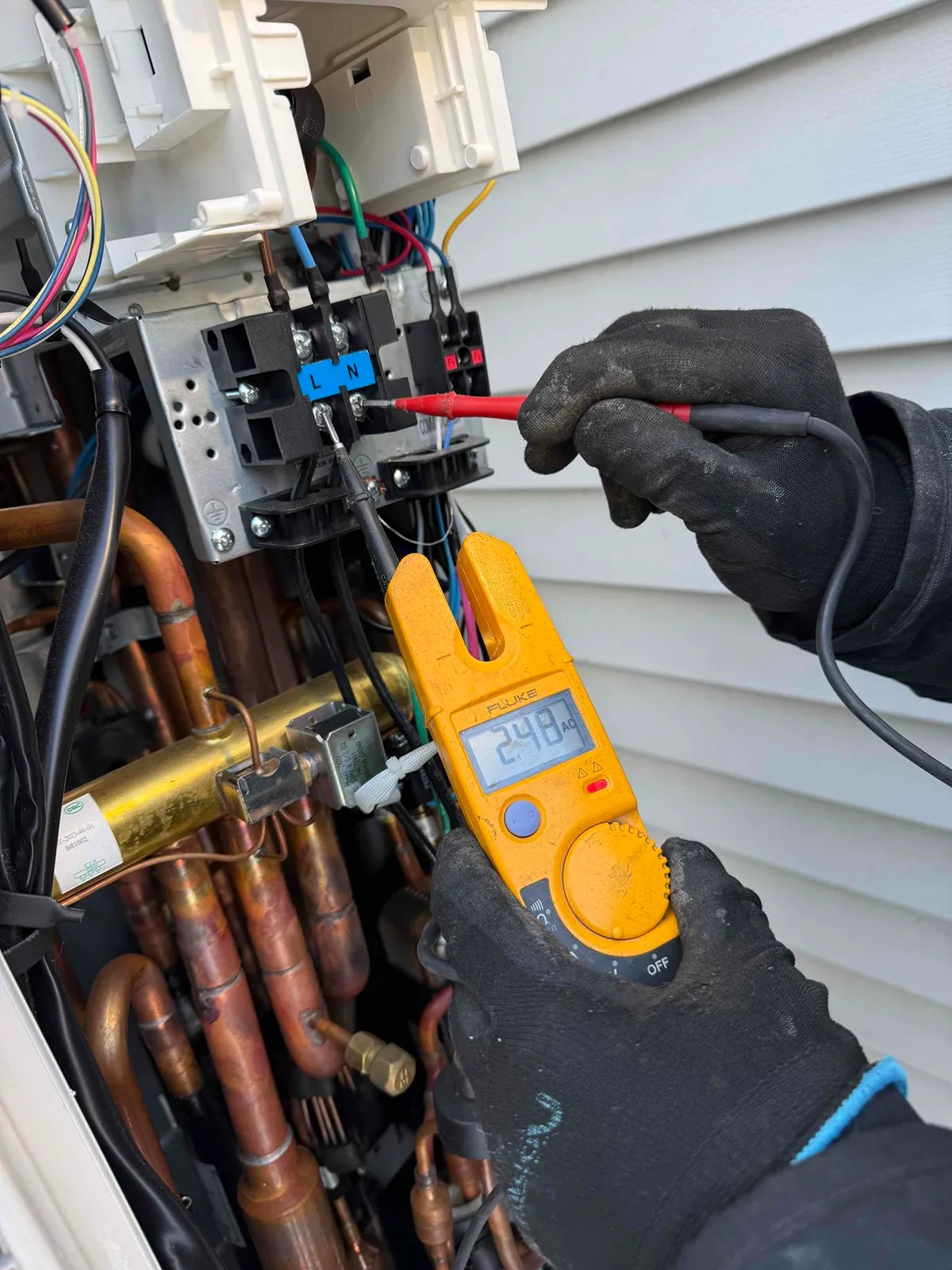 Electrician wearing protective gloves testing voltage at equipment terminals with a clamp meter